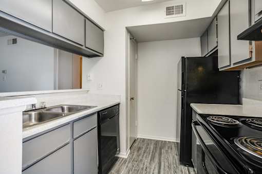 A black refrigerator sits in a kitchen with white cabinets and a stove top oven.