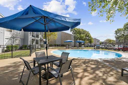 A blue umbrella is over a table and chairs by a pool.