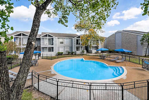 A pool surrounded by a black fence with trees in the foreground.