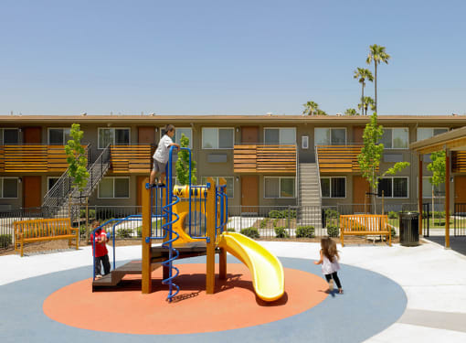 a playground with a slide and climbers in front of a building