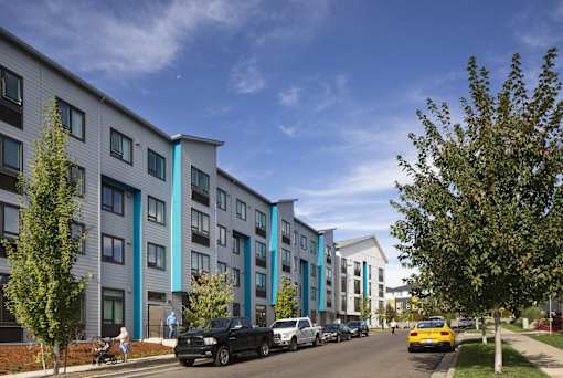 A row of modern apartment buildings with cars parked in front.
