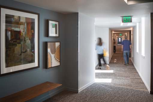 A hallway with a green exit sign and people walking.