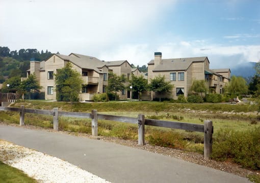 a path leading to a row of apartment buildings with trees and grass in the background