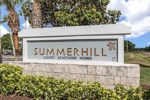 A sign for Summerhill Luxury Apartment Homes is displayed in front of a tree.