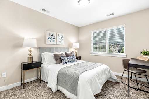A bedroom with a bed, a chair, and a table with a lamp on it.