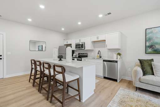 A kitchen with white cabinets and a white island with brown chairs.