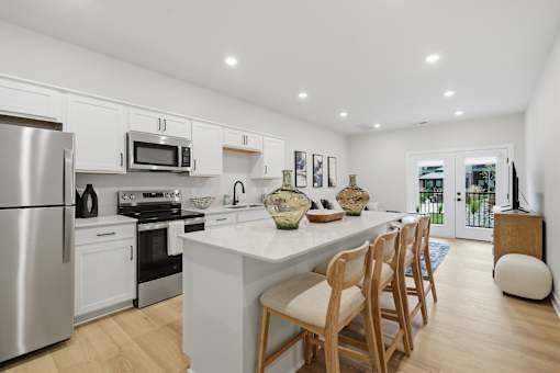 A modern kitchen with a white island and wooden chairs.