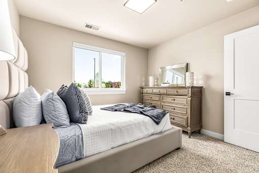 A bedroom with a bed, dresser, mirror, and window.