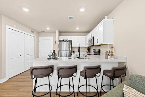 A kitchen with white cabinets and a bar area with brown stools.