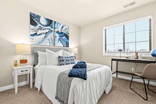 A bedroom with a large bed, a desk with a chair, and a painting on the wall.
