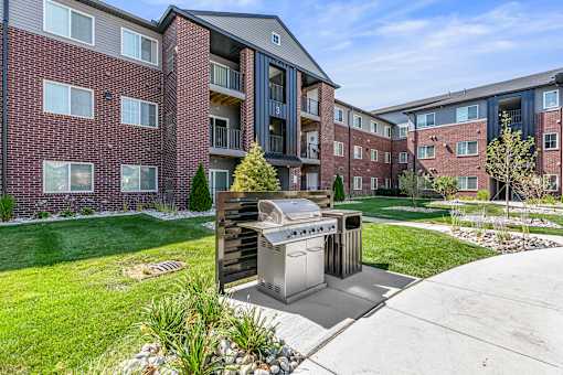 A modern outdoor kitchen with a grill and sink is situated in a grassy courtyard between two apartment buildings.
