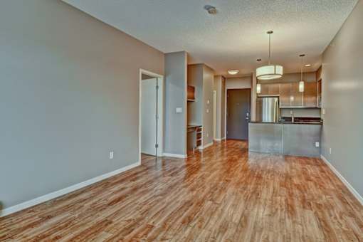 A room with wooden flooring and a kitchen area in the background.