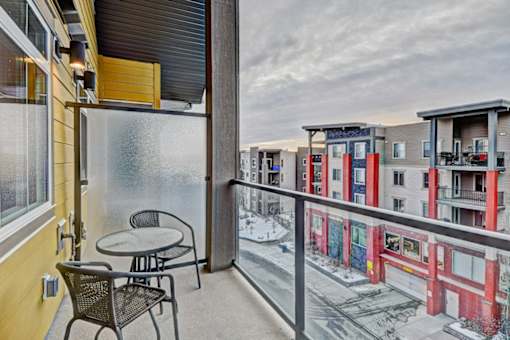 A balcony with a table and chairs overlooks a snowy street.
