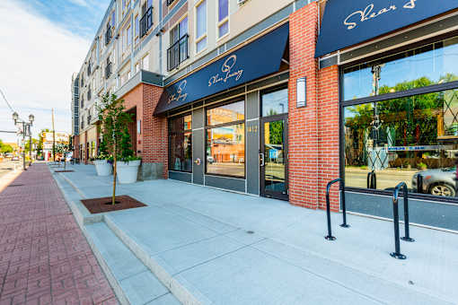 A brick sidewalk leads to a storefront with a blue awning.