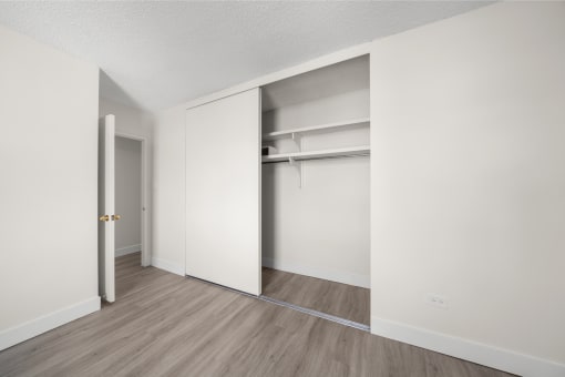 an empty room with white walls and wood flooring and a closet