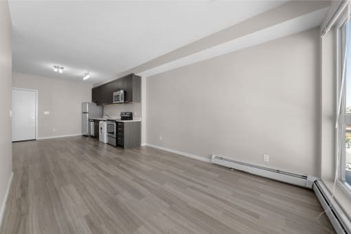 the living room and kitchen of an apartment with wood flooring and a large window