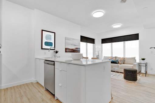 A modern kitchen with white cabinets and appliances, a framed picture on the wall, and a large window with blinds.