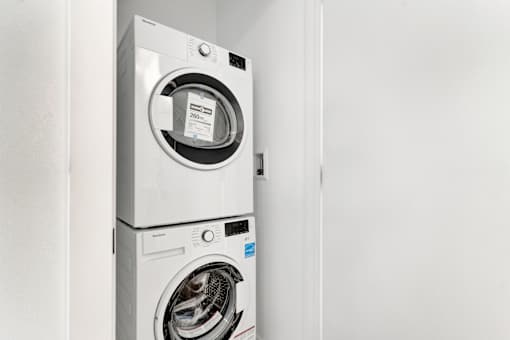A white front loading washing machine with a black door is in a white room.