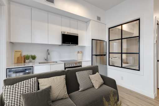 A modern living room with a grey couch and a kitchen area in the background.