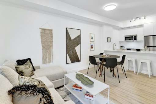 A modern living room with a white sofa, a coffee table, and a dining area in the background.