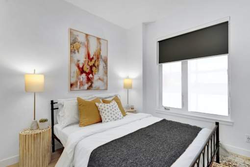 A bedroom with a large bed, two lamps, and a painting on the wall.