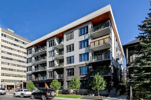 A modern multi-story apartment building with balconies and a parking lot in front.