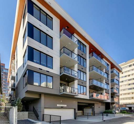 A modern multi-story residential building with balconies and a mix of window sizes.