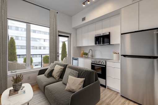 A modern kitchen with a grey couch and a stainless steel refrigerator.