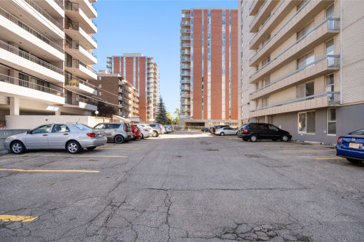 an empty parking lot with tall buildings on either side and cars parked
