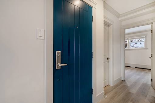 A blue door with a silver handle in a white hallway.