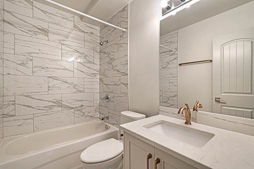 A white bathroom with a marble tile wall and a white toilet.