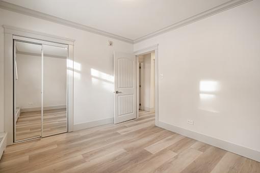 A room with a wooden floor and white walls, with a door and a window.