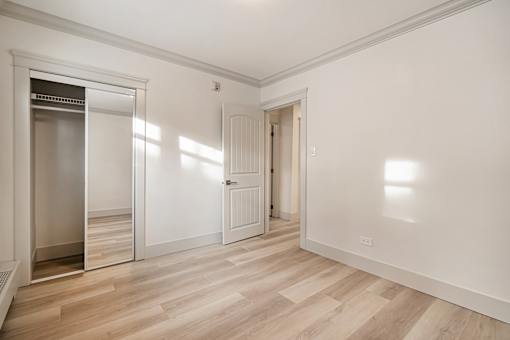 A room with a wooden floor and white walls, with a door on the left and a window on the right.