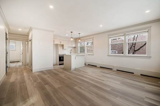 A spacious kitchen with wooden flooring and white walls.