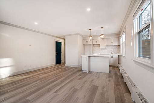 A room with wooden floors and white walls, with a window on the right side.