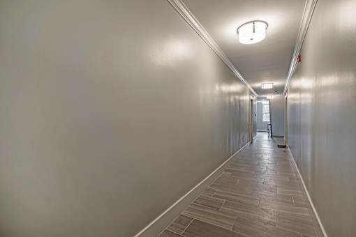 A long hallway with a light on the ceiling and a door at the end.