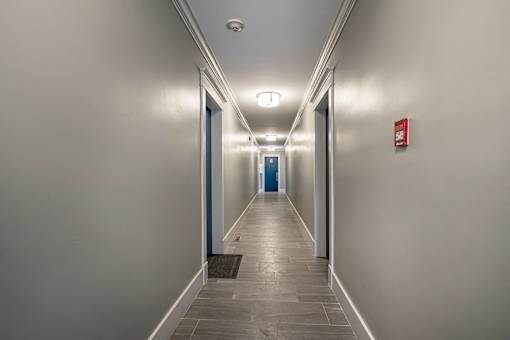 A long hallway with doors at the end and a fire extinguisher on the wall.