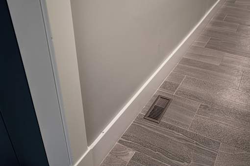 A corner of a room with a tiled floor and a drain in the floor.