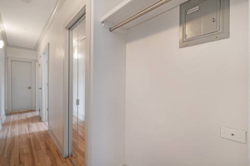 A long hallway with a door on the left and a vent on the wall.