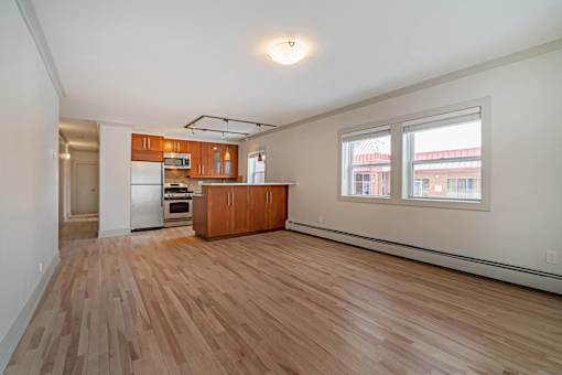A room with wooden floors and a kitchen area in the background.