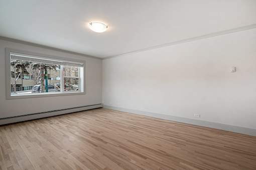 A room with wooden flooring and a window showing a view of trees and buildings outside.