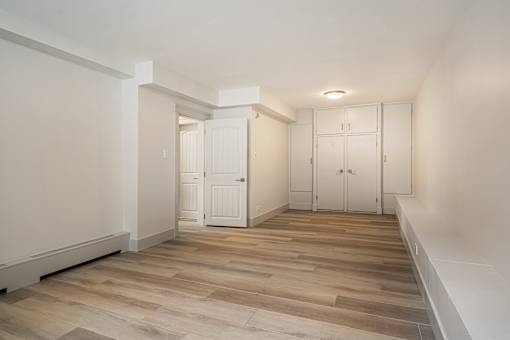 A room with white walls and wooden flooring with a white door on the left and a white wardrobe on the right.