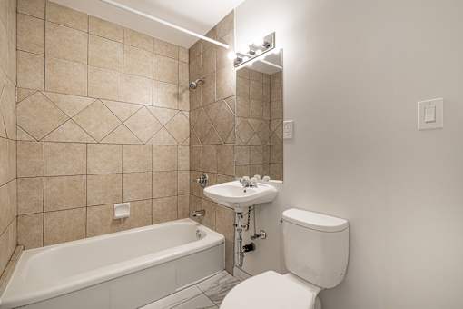 A white toilet sits next to a bathtub in a bathroom with beige tiled walls.