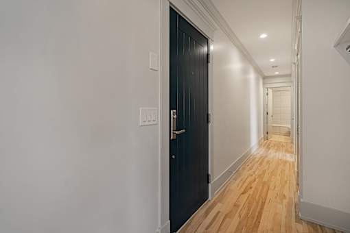A long hallway with a black door on the left and a wooden floor.