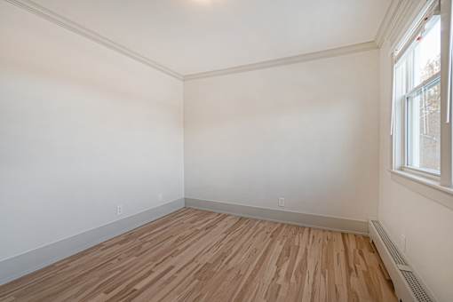 A room with wooden flooring and a window on the right side.