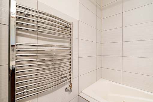 A white tiled bathroom with a white bathtub and a chrome towel rack.
