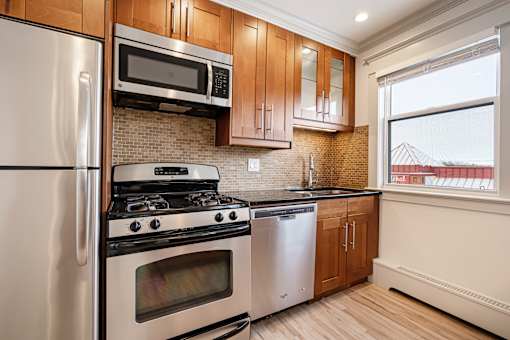 A kitchen with a stainless steel refrigerator, microwave, oven, and cabinets.