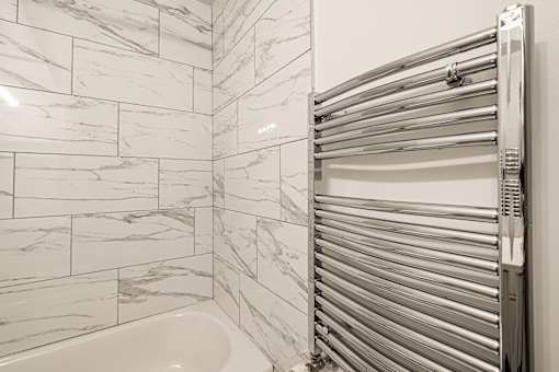 A white tiled bathroom with a closed towel warmer.