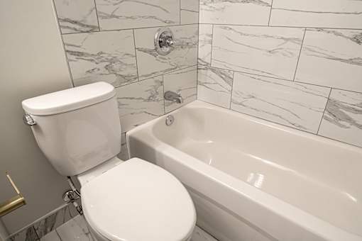 A white toilet sits next to a bathtub in a bathroom with marble tile walls.