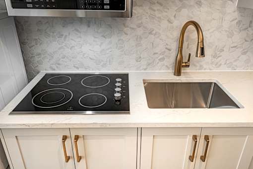 A kitchen with a black stove top and a sink with a gold faucet.